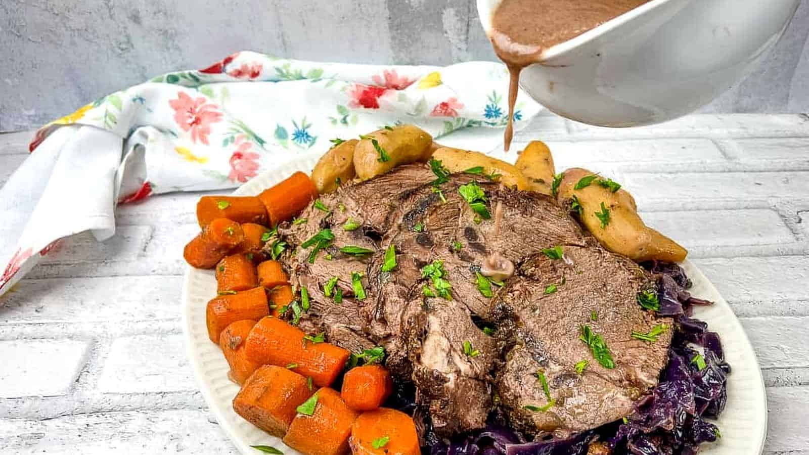 A plate of German pot roast beef with a sauce being poured over it.