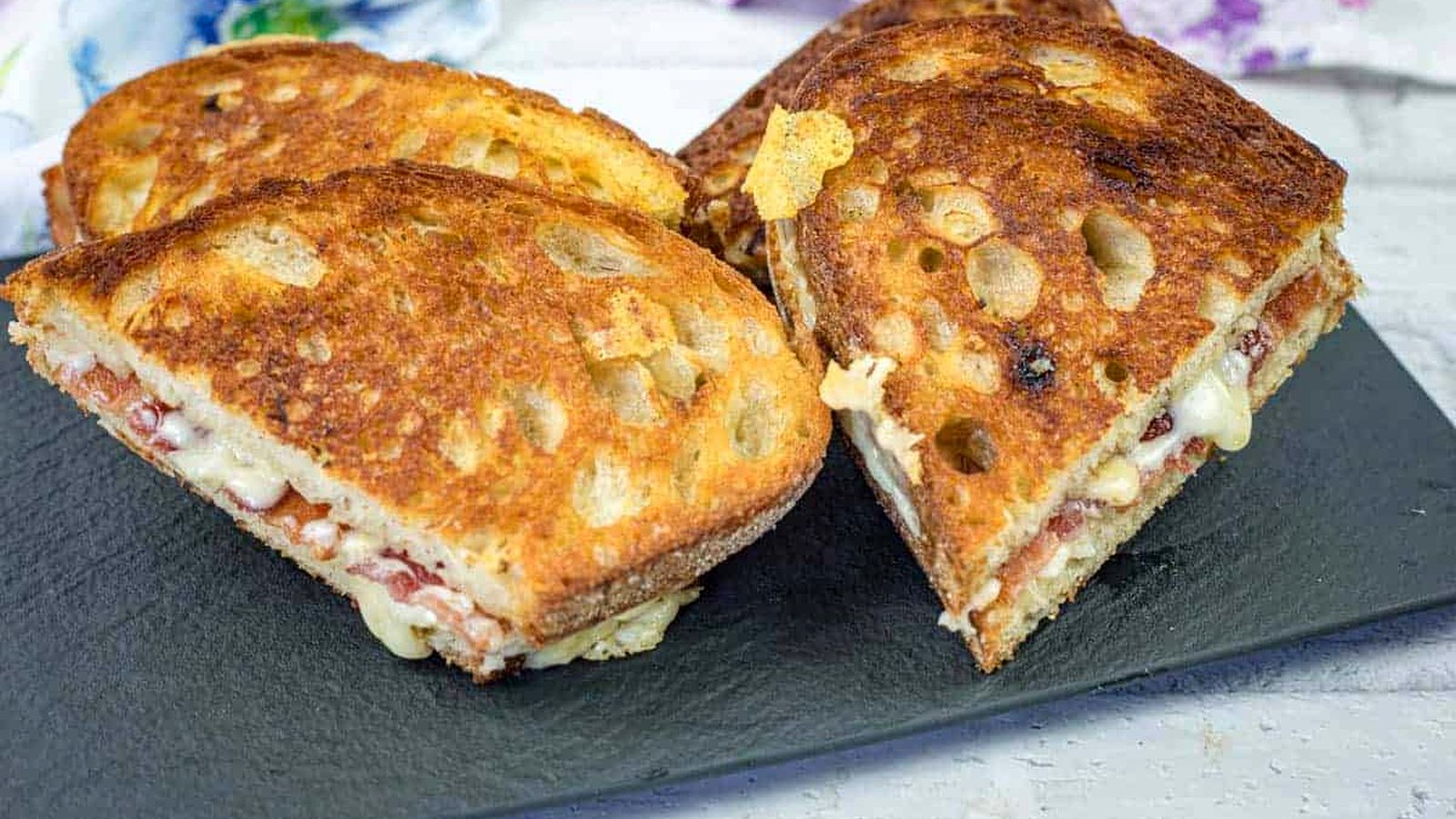 Four grilled cheese sandwiches with hot honey butter on a black slate serving board.