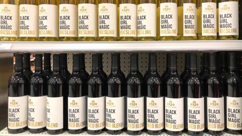 Shelves display bottles of Black Girl Magic Riesling on the top row and Black Girl Magic Red Blend on the bottom row, all with white labels and gold caps—showcasing standout selections from celebrated black-owned food brands.