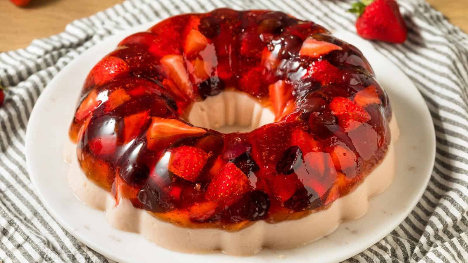 A gelatin dessert ring with visible strawberries and fruit pieces, served on a white plate atop a striped cloth.