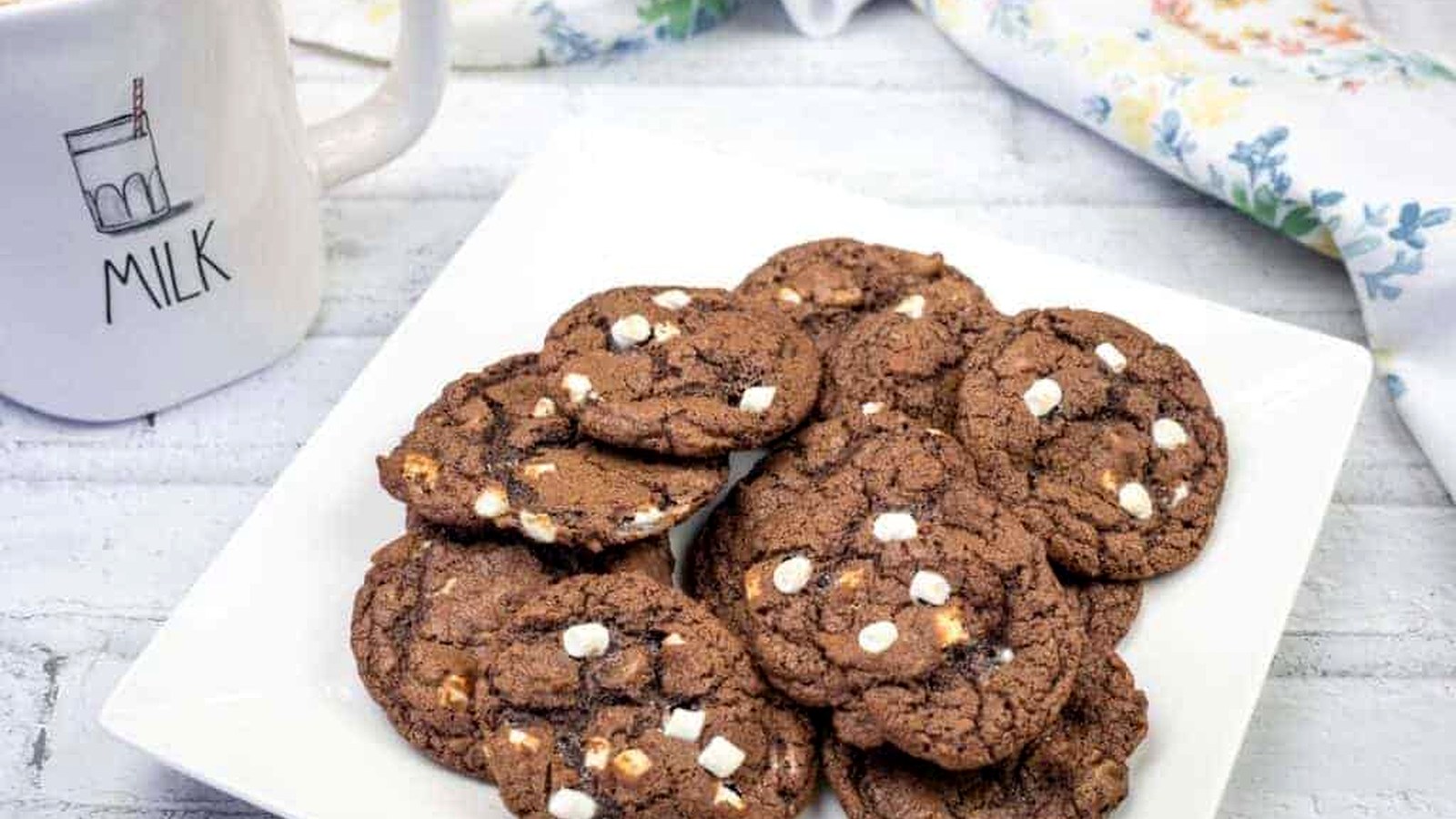 A white square plate with a stack of chocolate cookies featuring white chocolate chips.