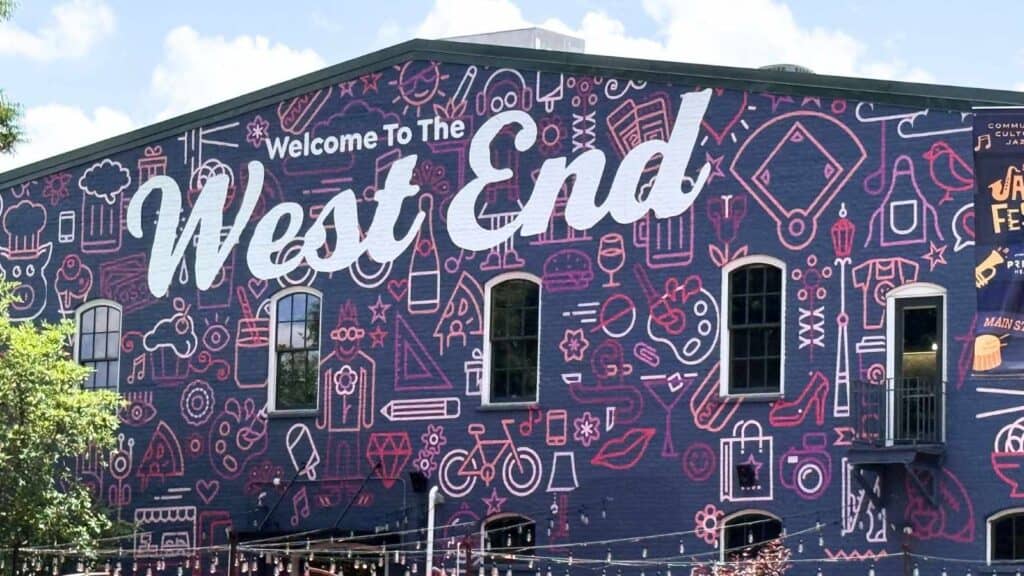 A large mural on a building reads "Welcome To The West End" with various outlined icons and a dark purple background.