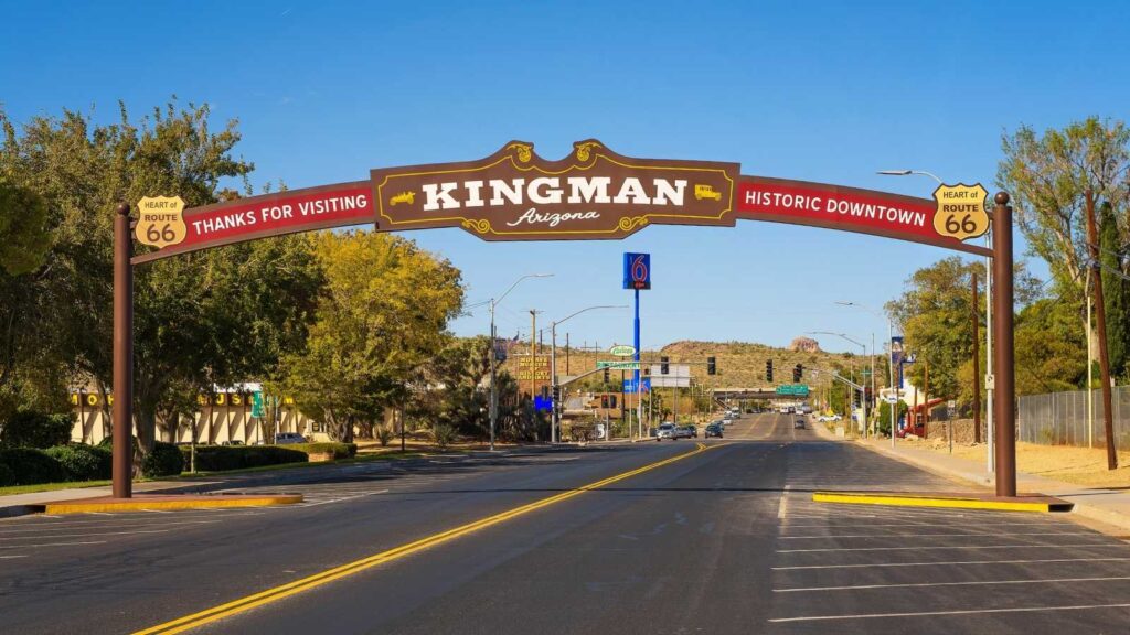 Large "Kingman, Arizona" sign spans a street, welcoming visitors to Historic Downtown, with Route 66 markers on each side and clear skies above—a scene as inviting as a Route 66 candy box waiting to be explored.