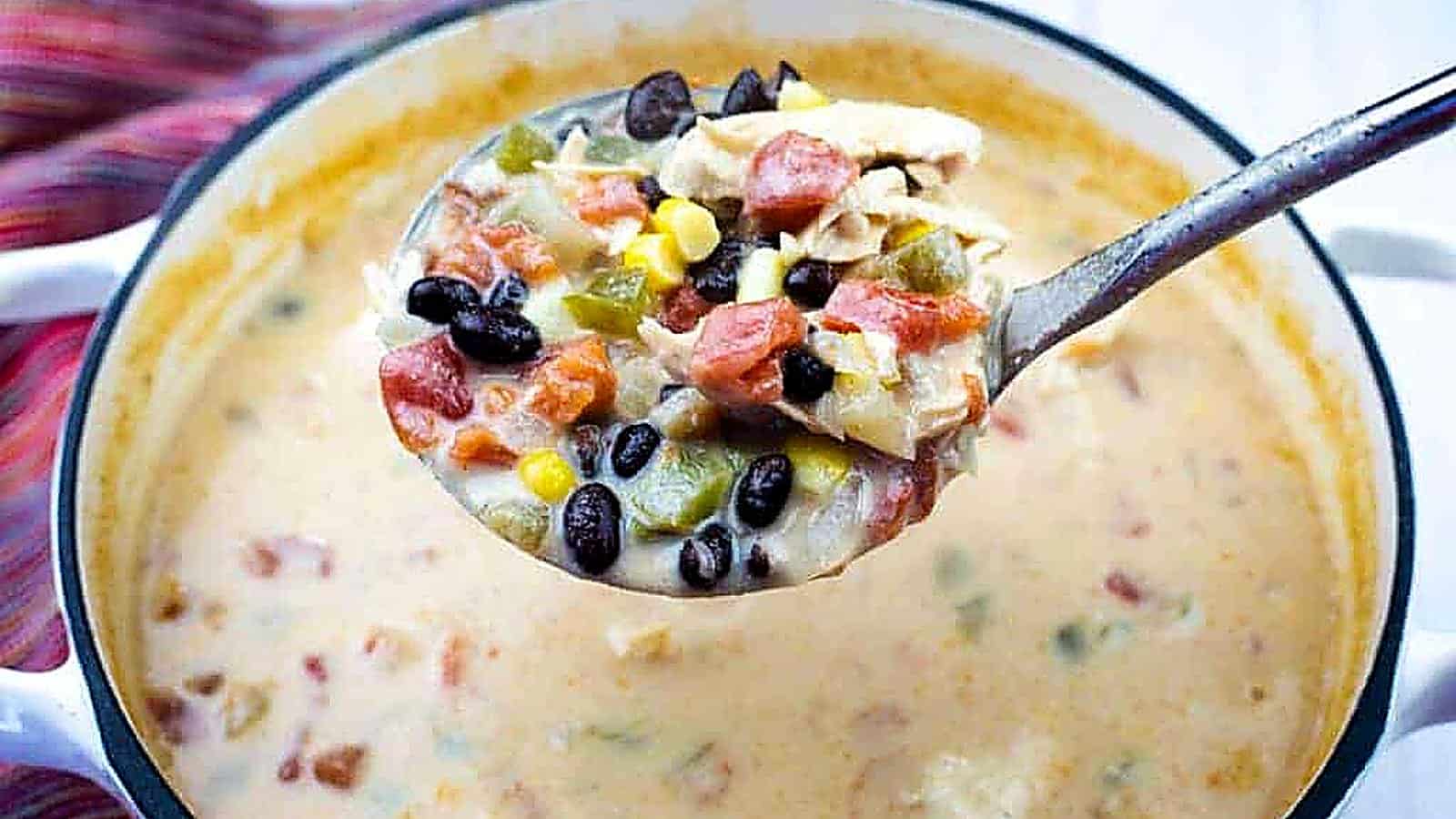 A ladle of creamy Chicken Tortilla  soup with black beans, corn, tomatoes, green peppers, and shredded chicken held over a pot.