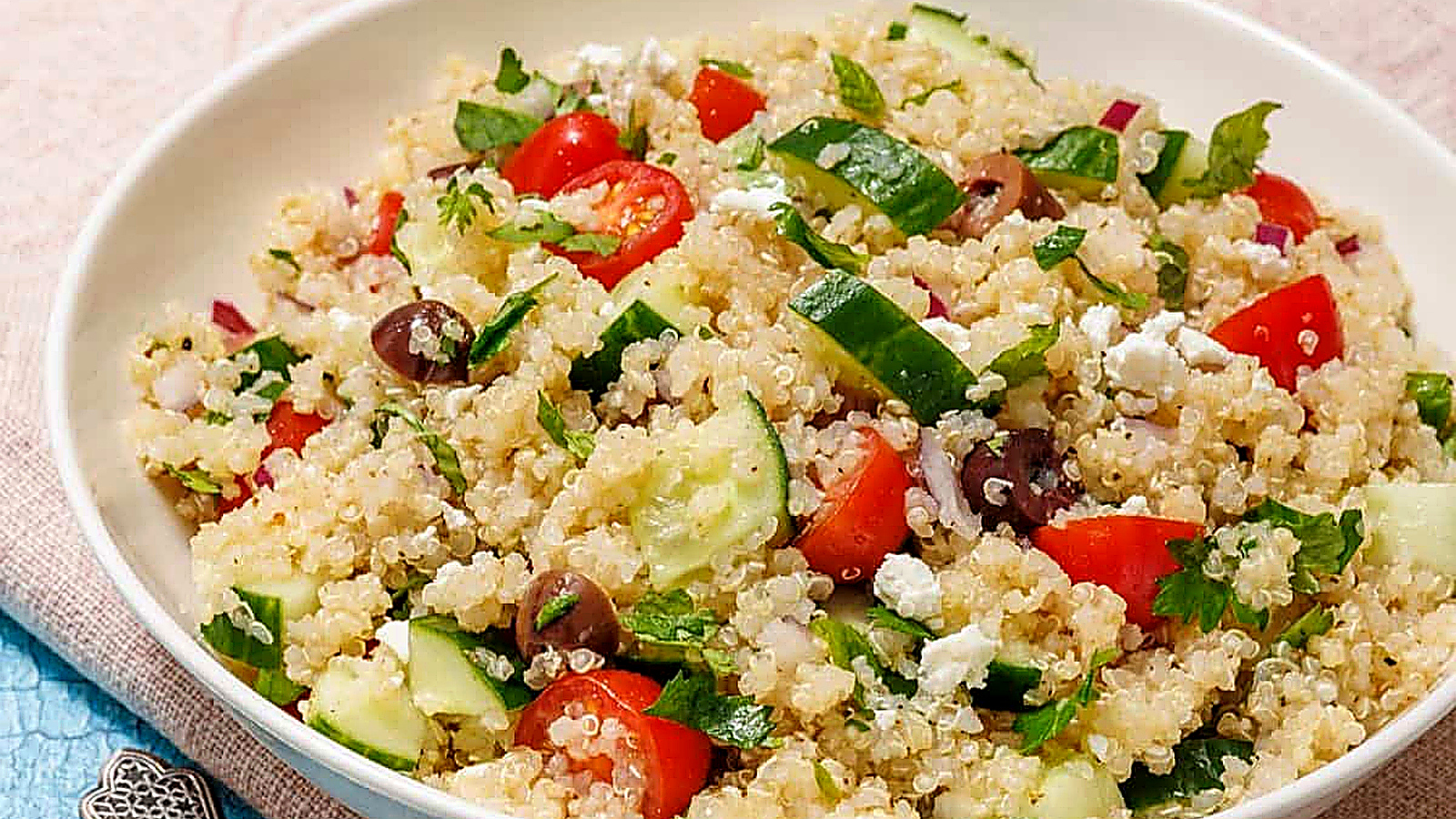 A white bowl of Mediterranean Quinoa Salad on a light blue tablecloth.