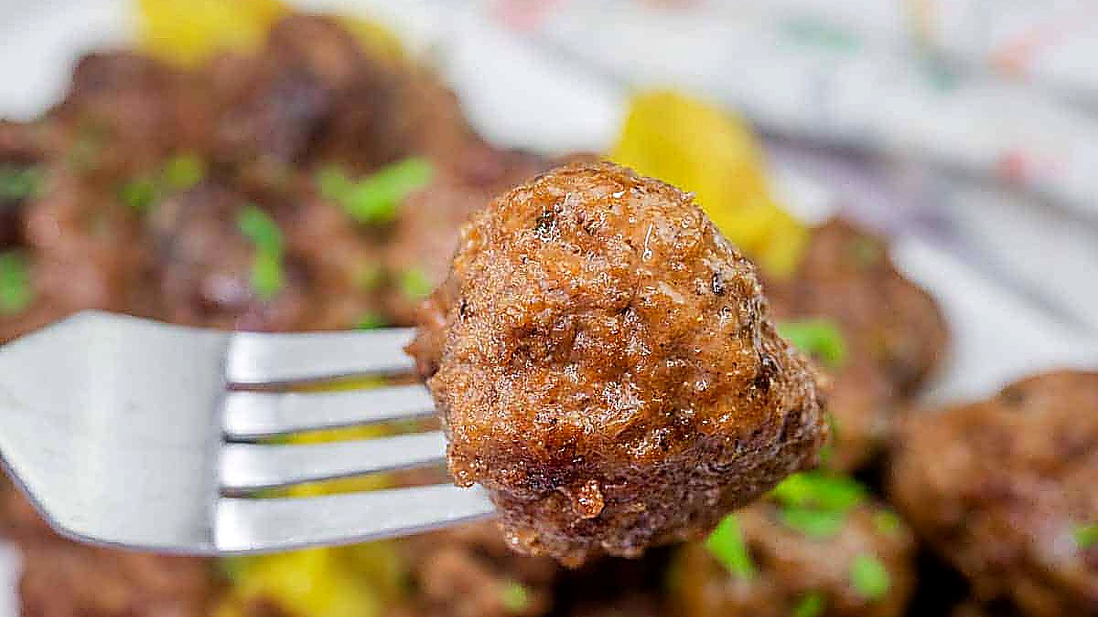 A close-up of a meatball on a fork, with more meatballs in the background.