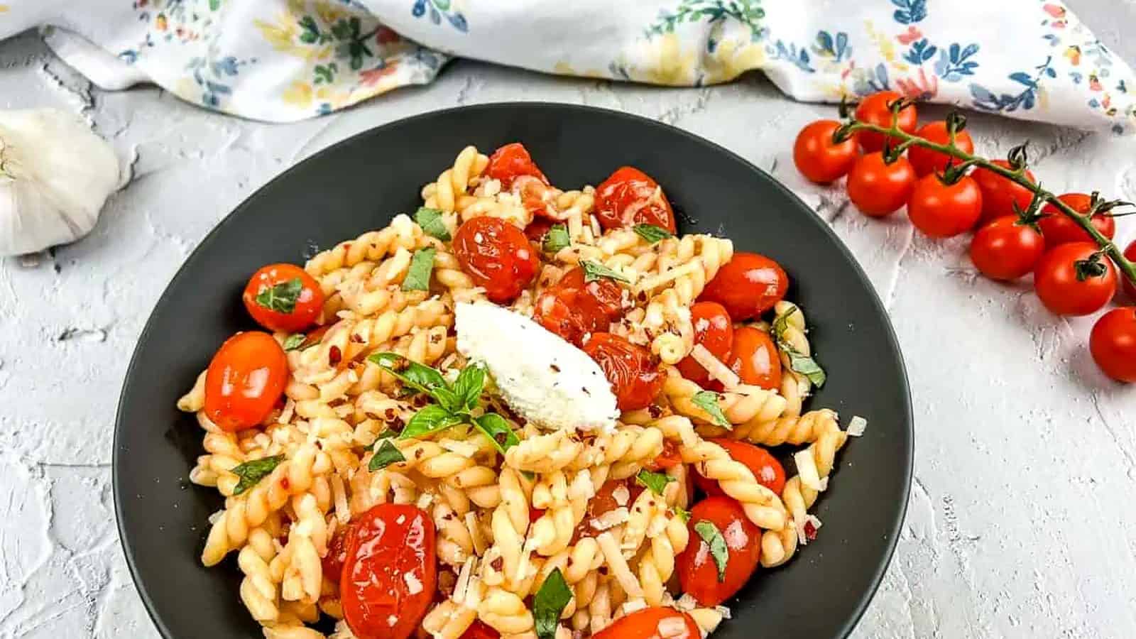 A bowl of Pasta with Fresh Cherry Tomato Sauce, alongside cherry tomatoes and garlic.