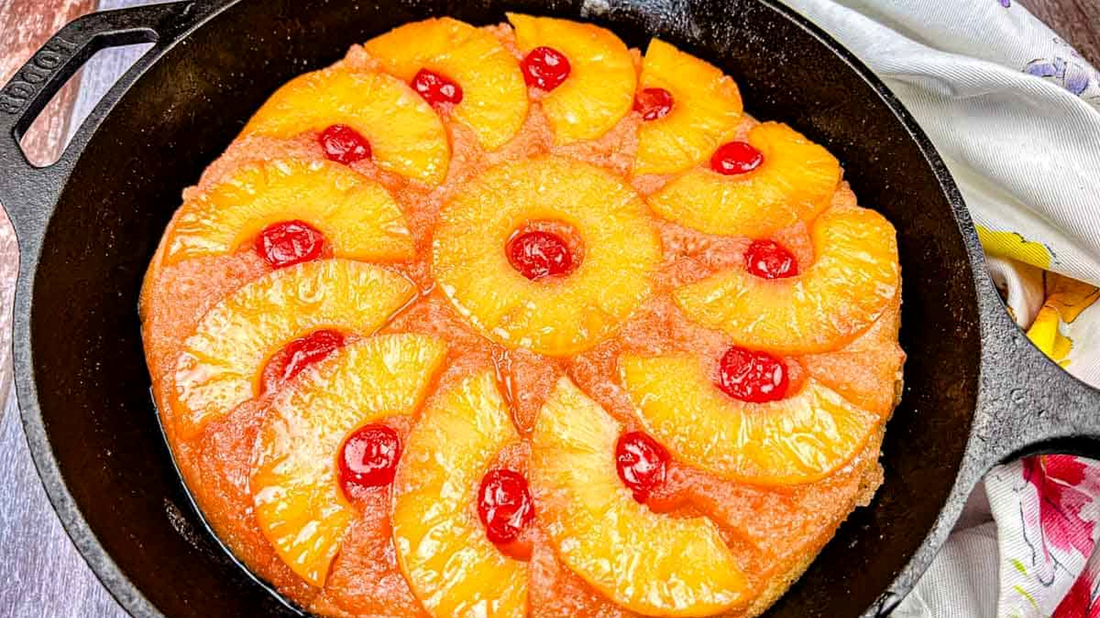 A pineapple upside-down cake with cherry toppings in a cast iron skillet.