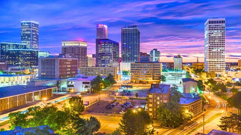 Downtown cityscape at dusk with illuminated buildings, streets, and a vibrant sky with purple and blue hues, evoking the nostalgic charm of a Route 66 candy box.