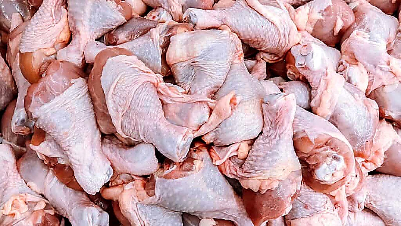 A large pile of raw chicken drumsticks and thighs stacked closely together.