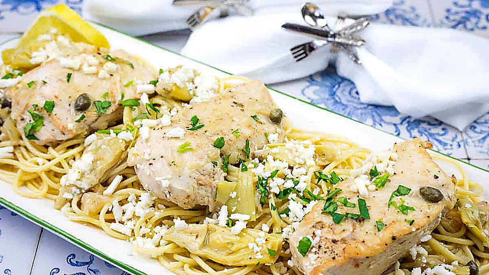 A dish of pasta topped with Skillet Chicken with Artichokes, Lemon, and Feta garnished with parsley.