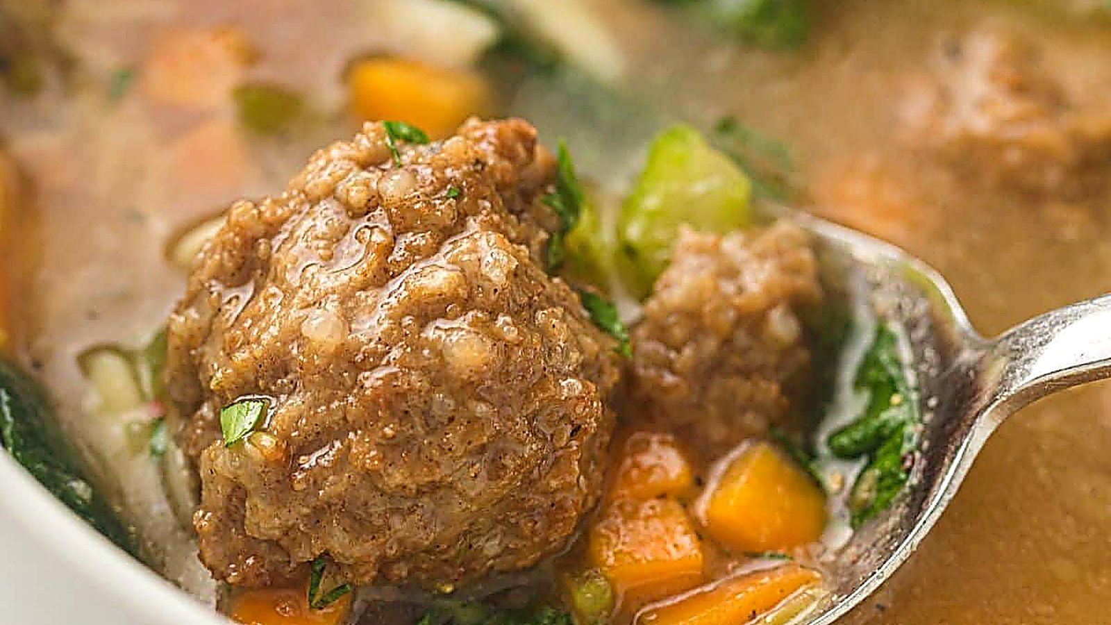 A close-up of a spoon holding a meatball in a bowl of Slow Cooker Italian Wedding Soup.