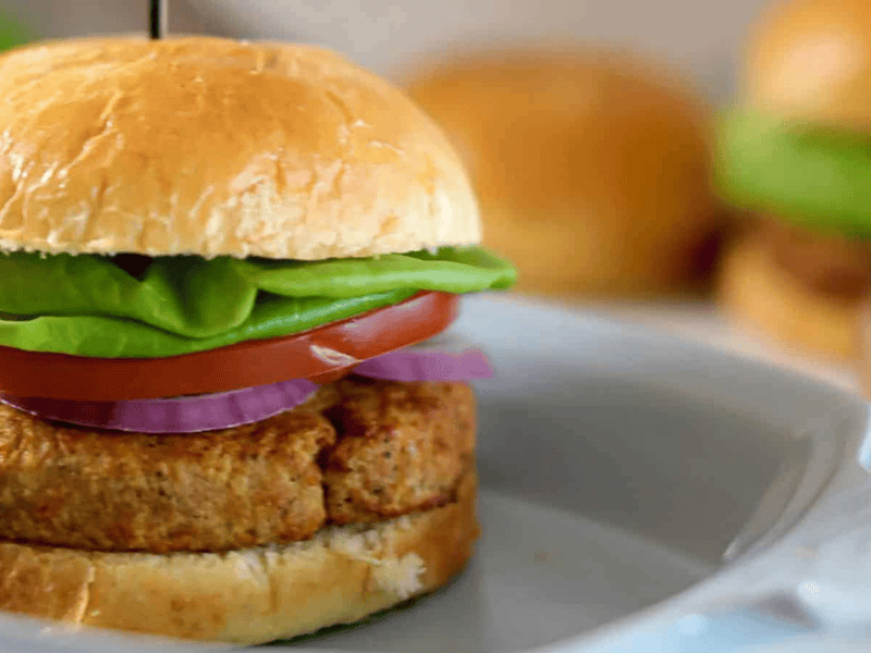 Tuna burger with lettuce, tomato, and onion on a bun, served on a white plate.