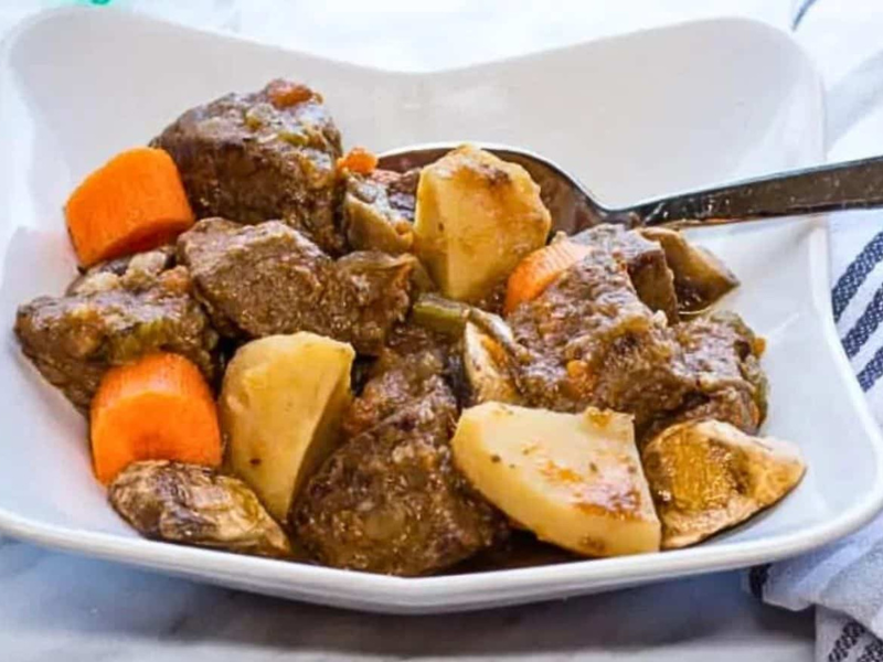 Beef stew in a white bowl with carrots and potatoes.