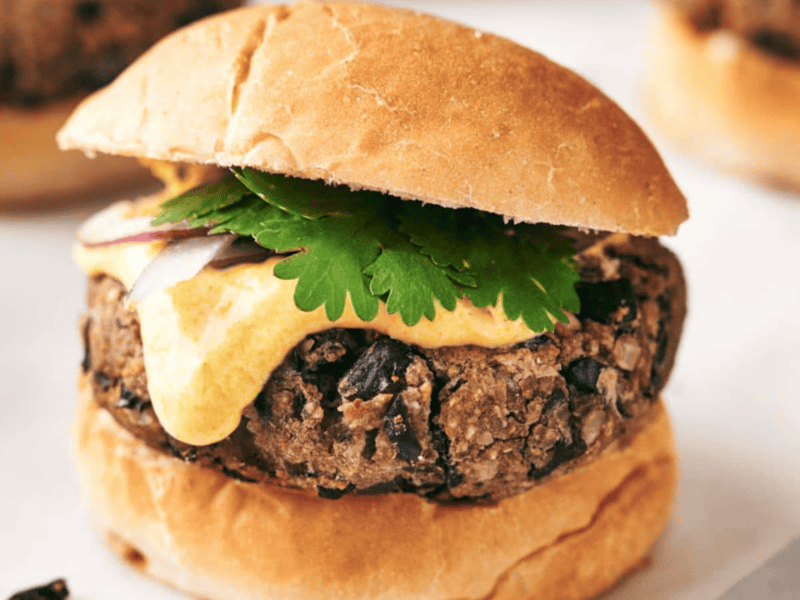 A black bean burger with a slice of cheese, cilantro, and red onion, served on a toasted bun.