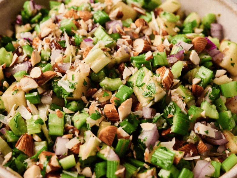 A bowl filled with chopped celery, red onion, apples, almonds, and fresh herbs.