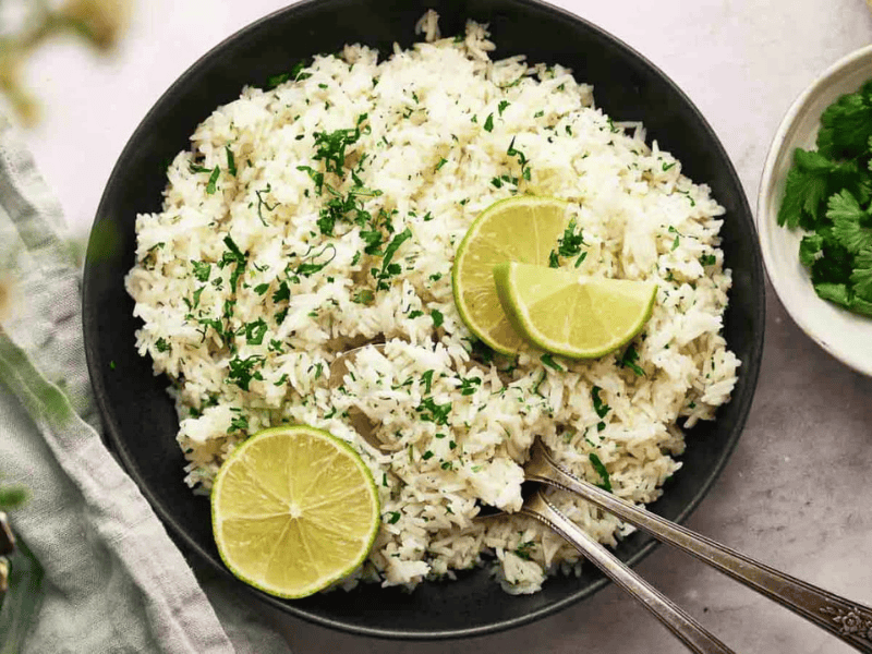 Chipotle rice in a bowl with sliced lime and spoons.