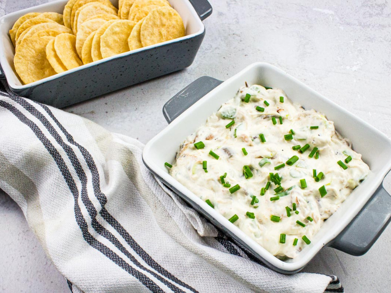 A bowl of cold crab dip with crackers and chives.