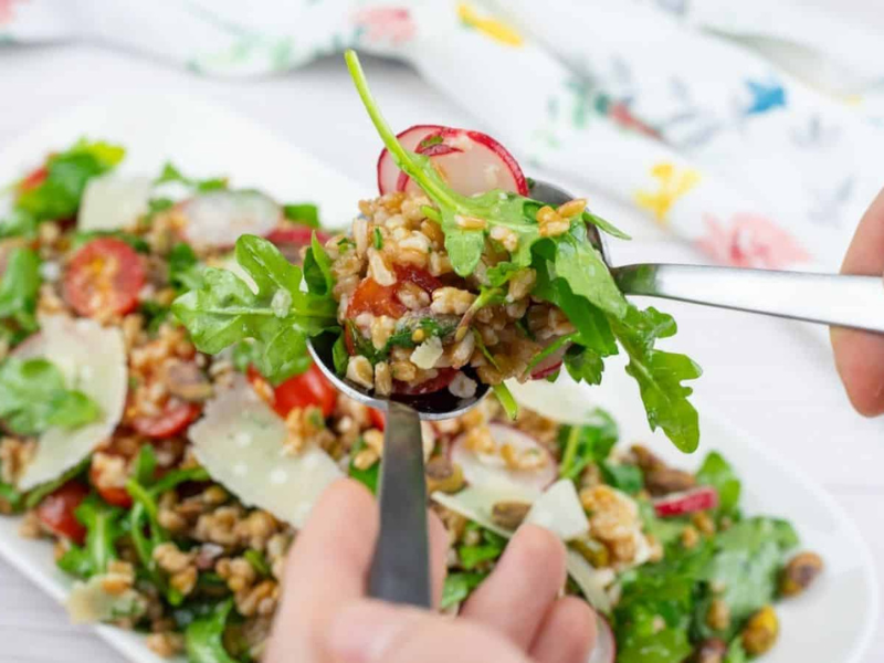 A close-up of a hand holding a spoonful of Copycat Charlie Bird’s Farro Salad over a plate of the same salad.