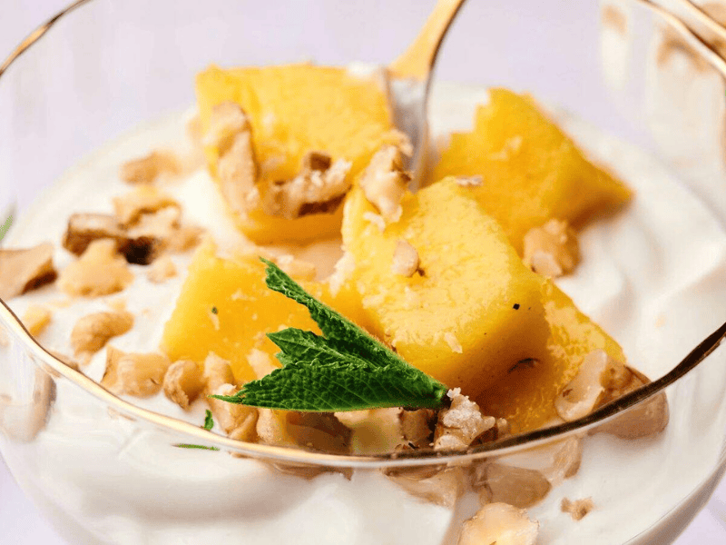 A glass dish with creamy yogurt, pineapple chunks, chopped walnuts, and a sprig of mint on top.