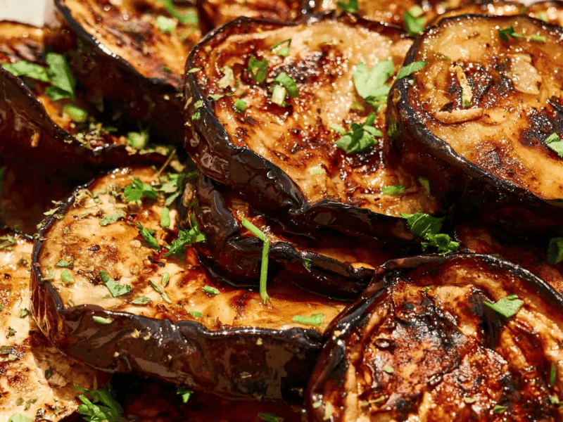 Close-up of grilled eggplant slices garnished with chopped herbs and a glossy glaze.