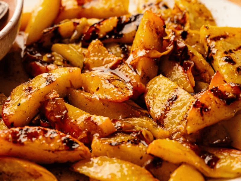 Close-up of grilled peach slices with caramelized, slightly charred edges on a white plate.