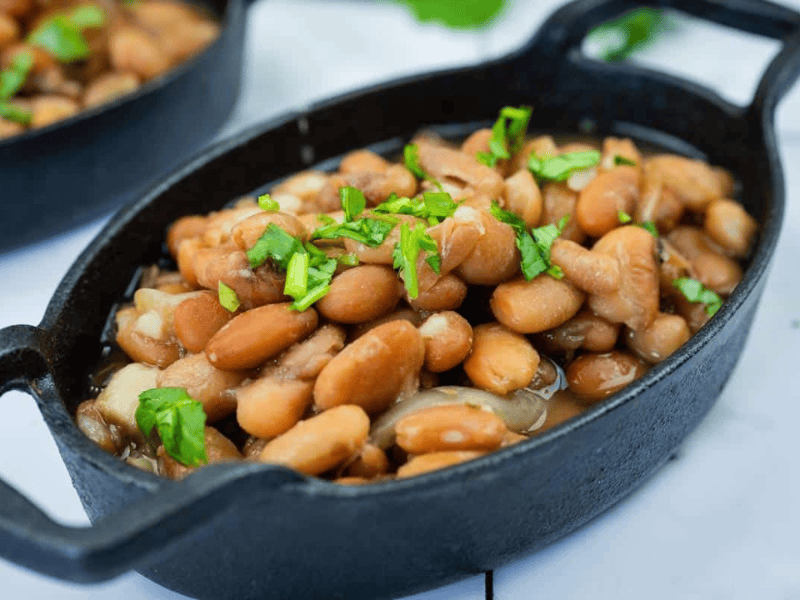 A black oval dish filled with Instant Pot Charro Beans topped with chopped cilantro.