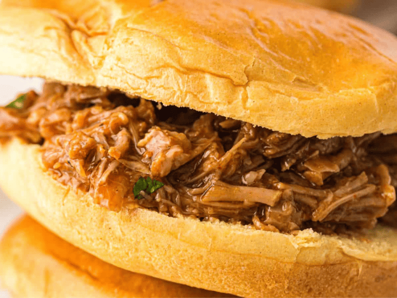 A close-up of a pulled pork sandwich on a soft bun, filled with shredded, saucy pork.