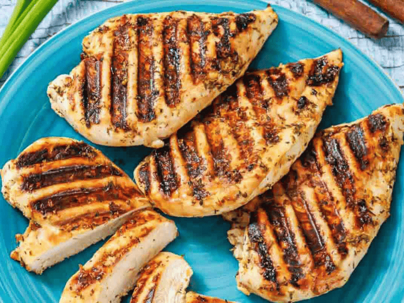 Grilled chicken breasts with visible grill marks arranged on a blue plate, some pieces sliced to show the cooked interior.