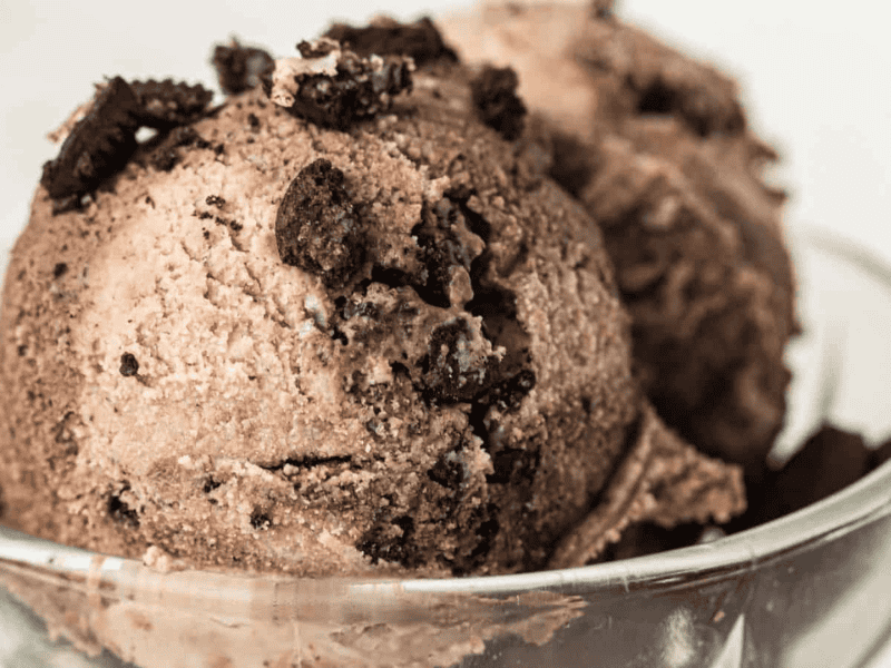 Two scoops of chocolate ice cream with crumbled chocolate cookies on top, served in a clear glass bowl.