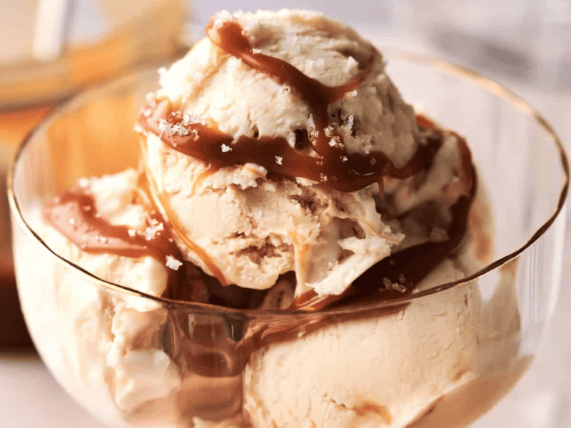 A glass bowl filled with scoops of vanilla ice cream topped with caramel sauce and a sprinkle of sea salt.