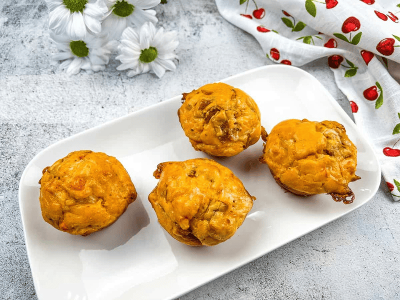 Four pizza muffins on a white plate with flowers.