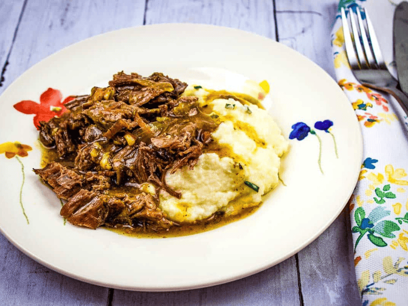 A plate of pot roast with bacon and mashed potatoes with gravy.