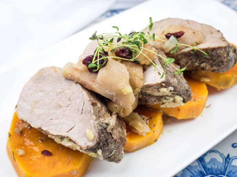 Sliced slow cooker pork roast with sweet potatoes & apples on a white plate.
