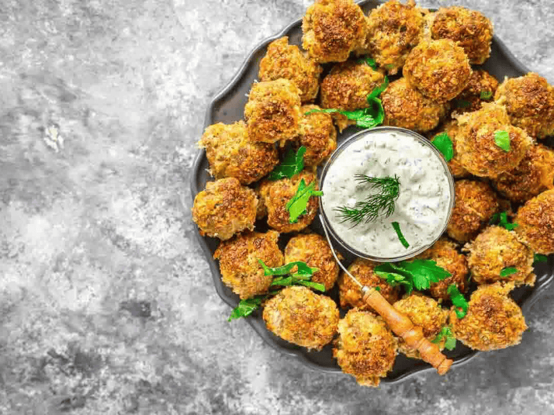 Sausage balls garnished with parsley around sauce.