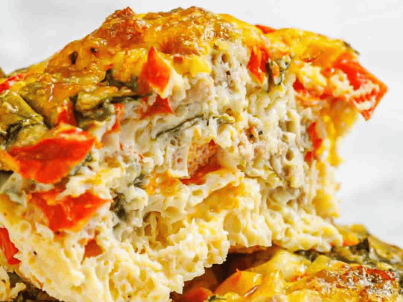 Close-up of a sliced egg muffin with visible chunks of red bell pepper, spinach, and bits of sausage.