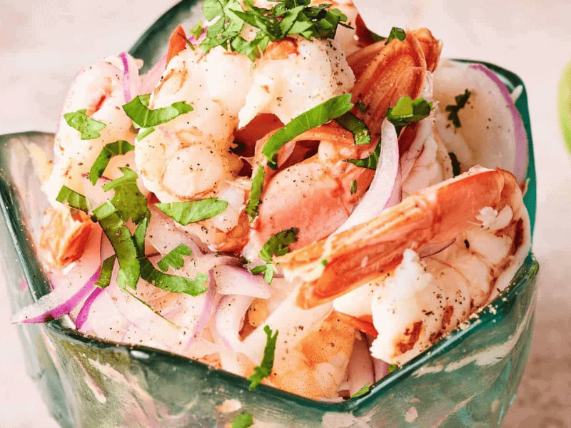 A close-up of shrimp ceviche with sliced red onions and chopped cilantro, served in a decorative green bowl.