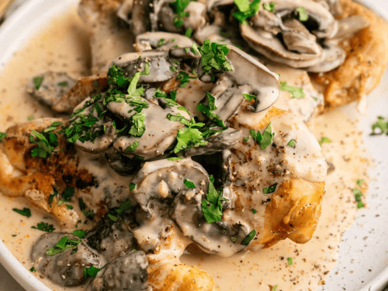 Plate of chicken covered in a creamy mushroom sauce, garnished with chopped parsley.