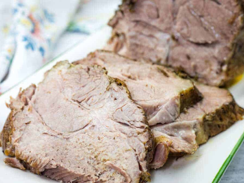 Sliced Herb-Crusted Pork Roast on a rectangular white plate with a floral napkin in the background.