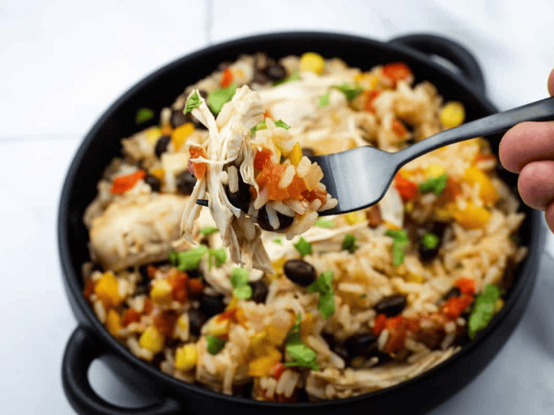 A close-up of a fork holding a bite of Slow Cooker Santa Fe Chicken over a bowl with the same mixed dish.