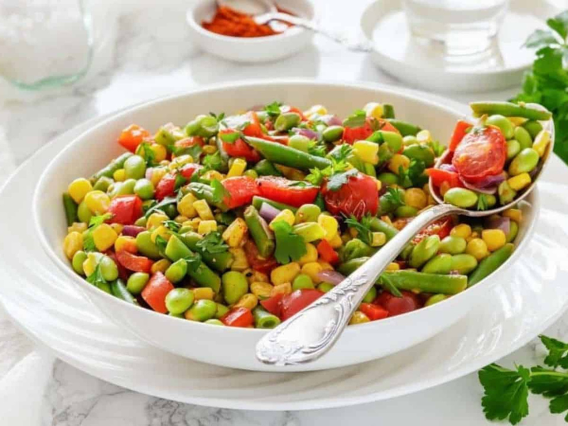 A white bowl filled with Southern Succotash with a serving spoon resting on the side.