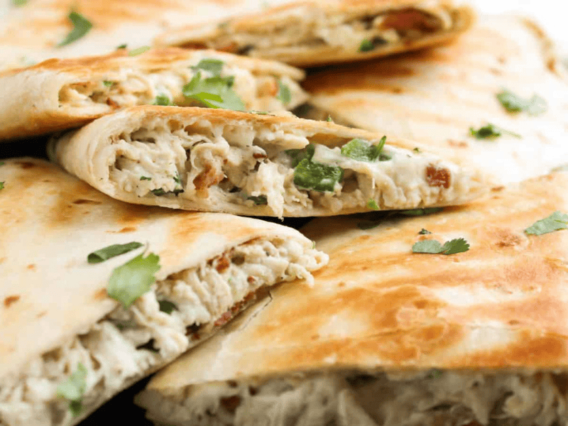 Close-up of folded tortillas filled with chicken, cheese, and herbs, garnished with cilantro.