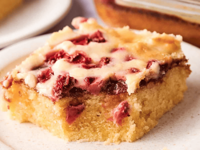 A slice of cherry-topped cake with a creamy layer, served on a white plate.