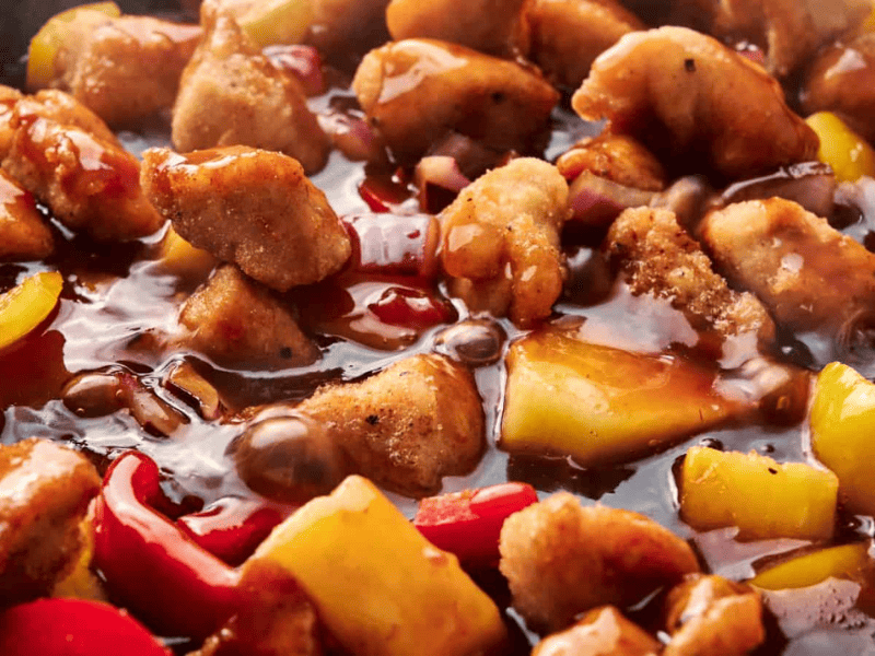 Close-up of sweet and sour chicken with bell peppers and pineapple chunks in a thick sauce.