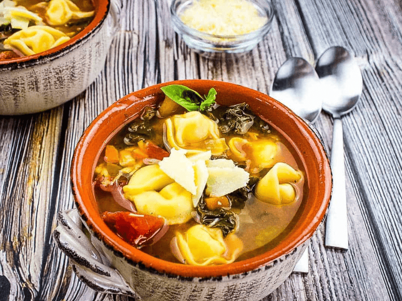 Tortellini Soup with Kale & Chicken in a bowl on a wooden table.