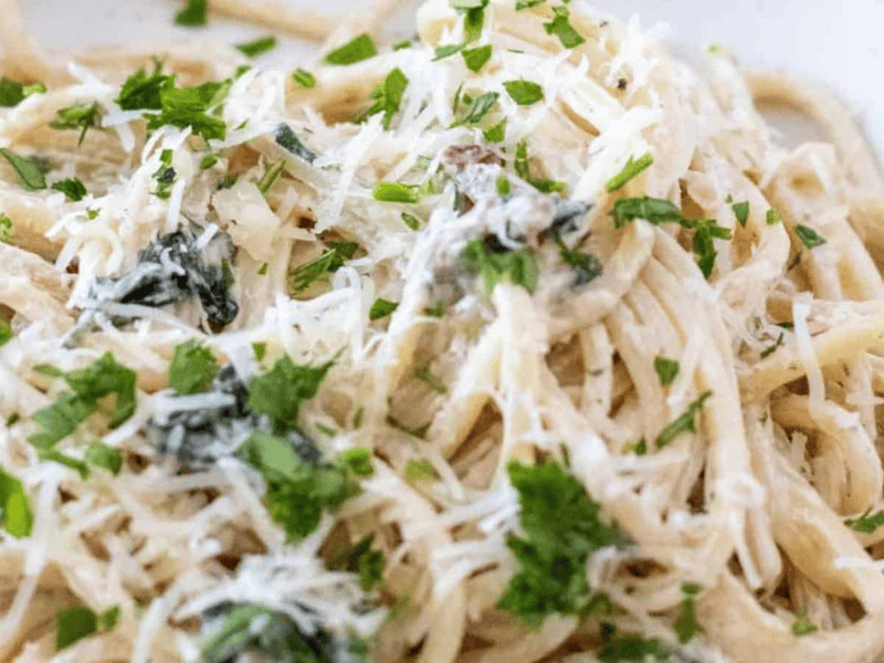 A close-up of a plate of Creamy Tuscan Pasta topped with a rich white sauce, grated cheese, and garnished with chopped parsley.