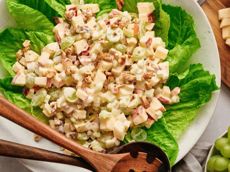 Waldorf salad on a bed of lettuce, with salad servers resting on top.