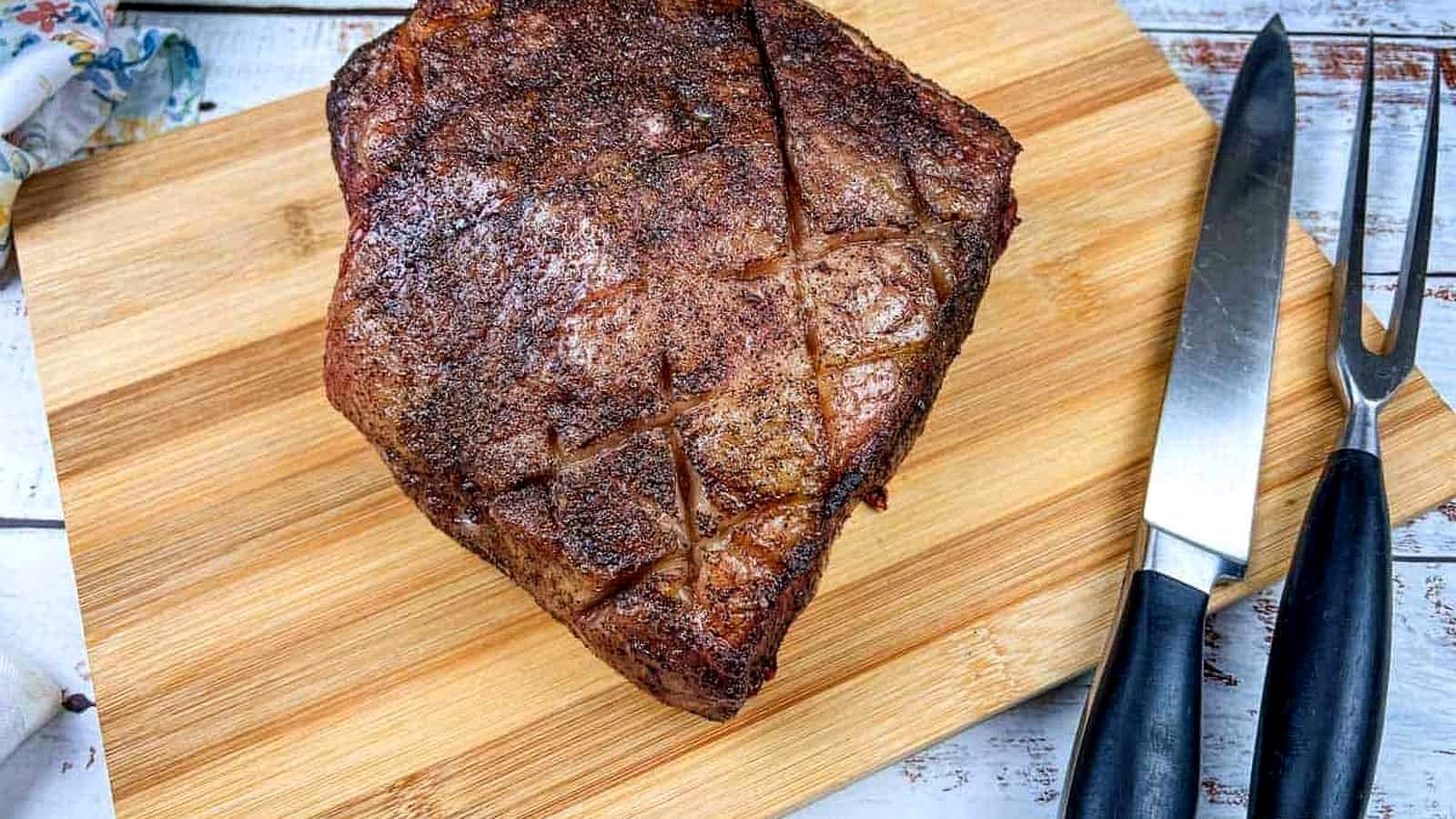 A piece of smoked New York strip roast meat on a cutting board next to a knife.