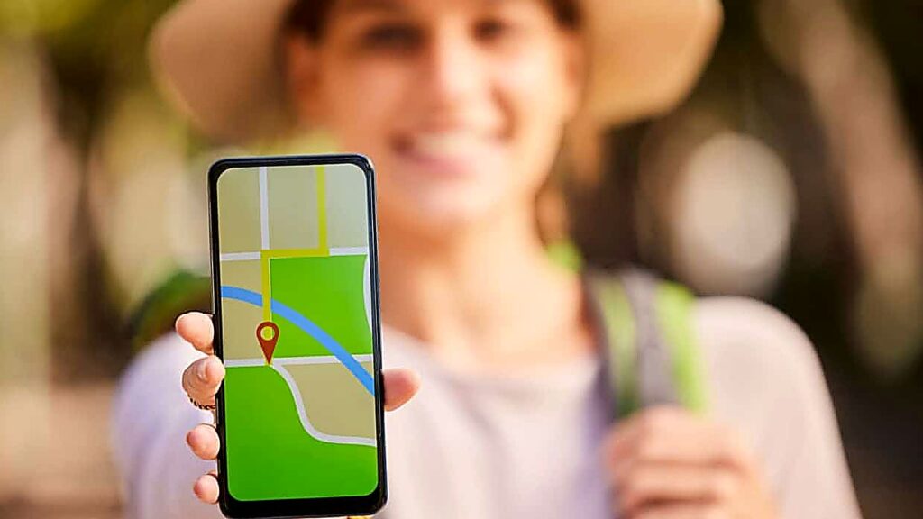 A person participates in a scavenger hunt, holding a smartphone displaying a digital map with a red location pin. The person's face is blurred, and the outdoors background is out of focus.