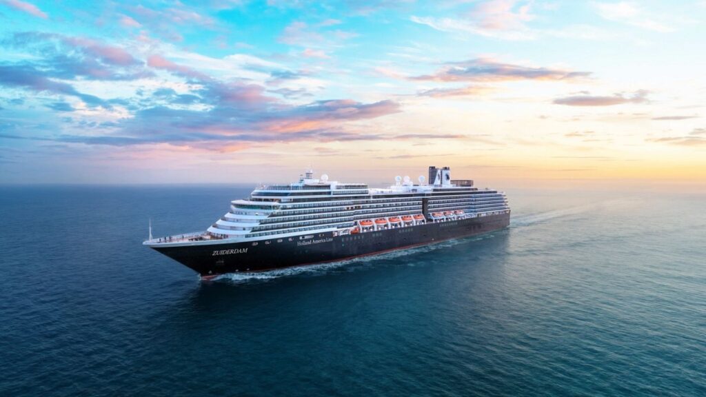 A large cruise ship sails on calm ocean waters at sunset under a partly cloudy sky.